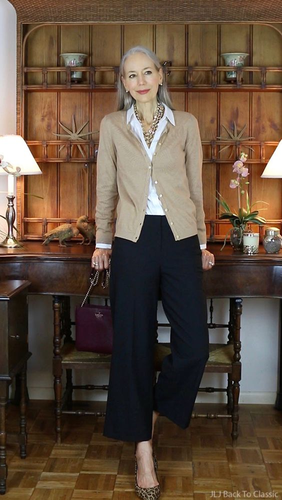 A woman over 50 is posing with a relaxed, self assured, quiet authority. She is wearing a nice, simple outfit with an oatmeal colored cardigan that exemplifies the Classic style archetype.